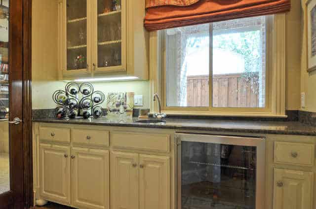 Wet bar with white cabinets, a beverage fridge, and a granite countertop topped with an iron wine rack.