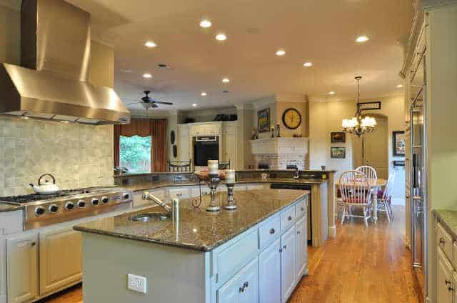 The kitchen is equipped with granite countertops, white cabinets, a two-tier peninsula, and a center island fitted with a round sink.