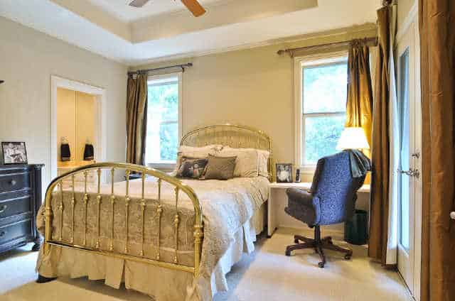 Another bedroom with a tray ceiling, a skirted bed, dark wood dresser, and a white desk paired with a swivel chair.