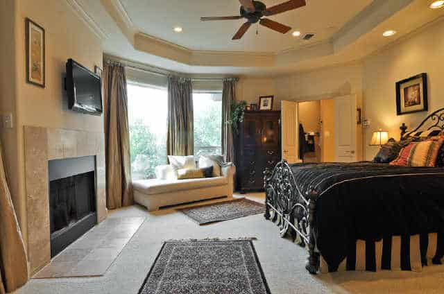 Another bedroom with a tray ceiling, a skirted bed, dark wood dresser, and a white desk paired with a swivel chair.