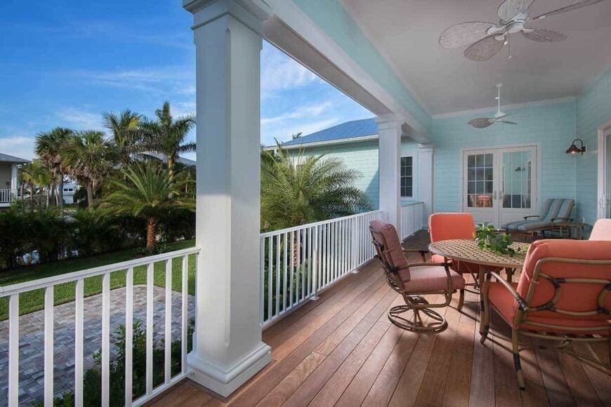 The covered porch is filled with cushioned seats, a round perforated table, and a pair of ceiling fans.