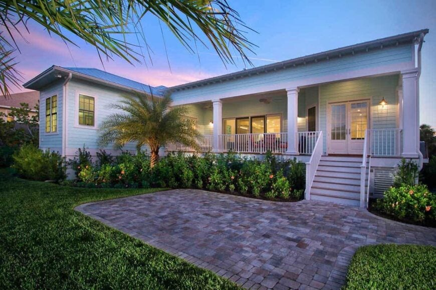 Rear exterior view showing the covered lanai and an open patio surrounded by lush green lawn and plants.