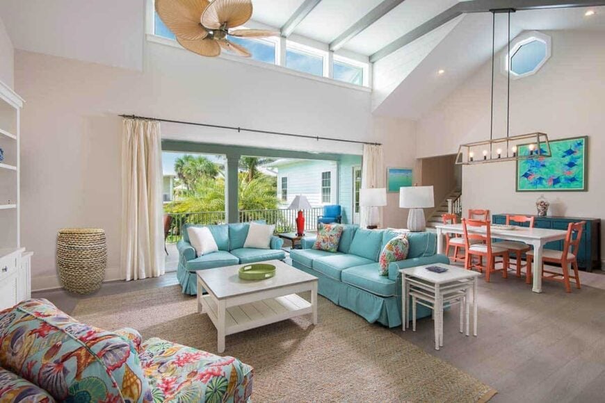Shared dining and living room with blue skirted sectionals, a patterned armchair, white tables, a jute area rug, and a rectangular dining set.