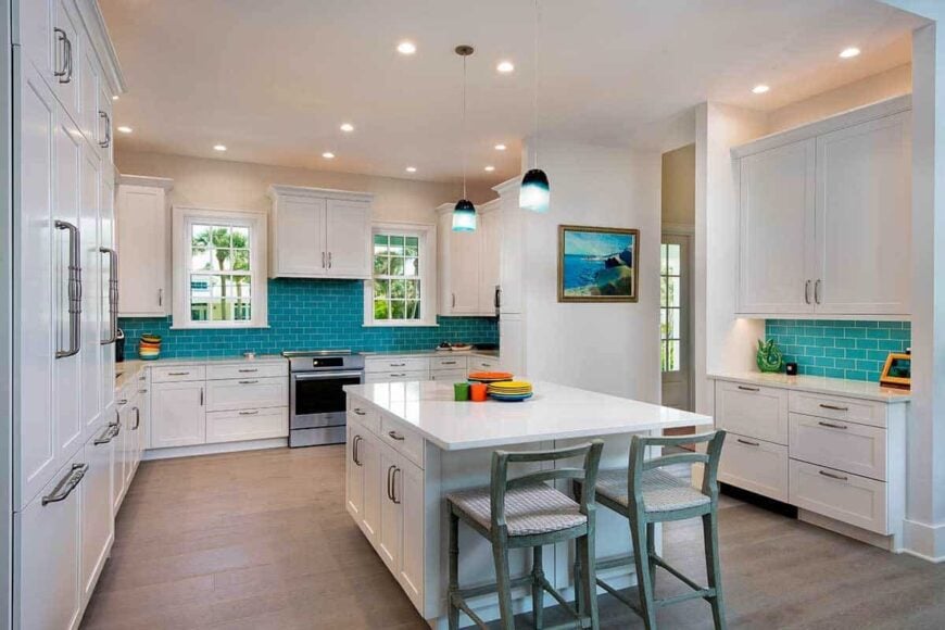 The kitchen is equipped with marble countertops, white cabinets, a breakfast island, and blue subway tile backsplash that adds a pop of color into the area.
