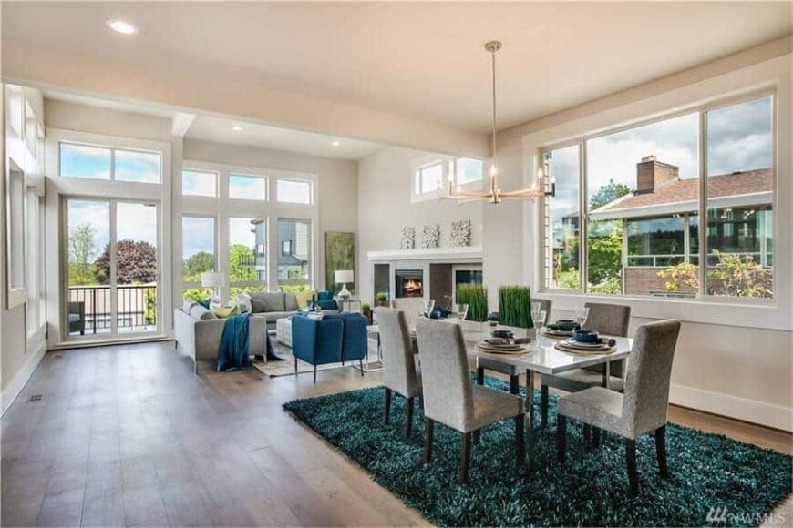 A farther view shows the dining area with a contemporary chandelier, gray upholstered chairs, and a rectangular dining table sitting on a shaggy area rug.
