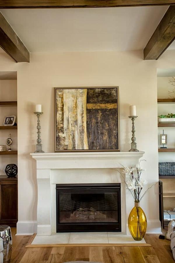 A large glass vase, candle holders, and a framed painting complement the glass-enclosed fireplace.