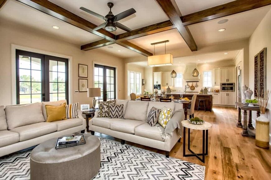 The living area has beige sectionals, round tables, and a tufted ottoman that sits on a chevron area rug.