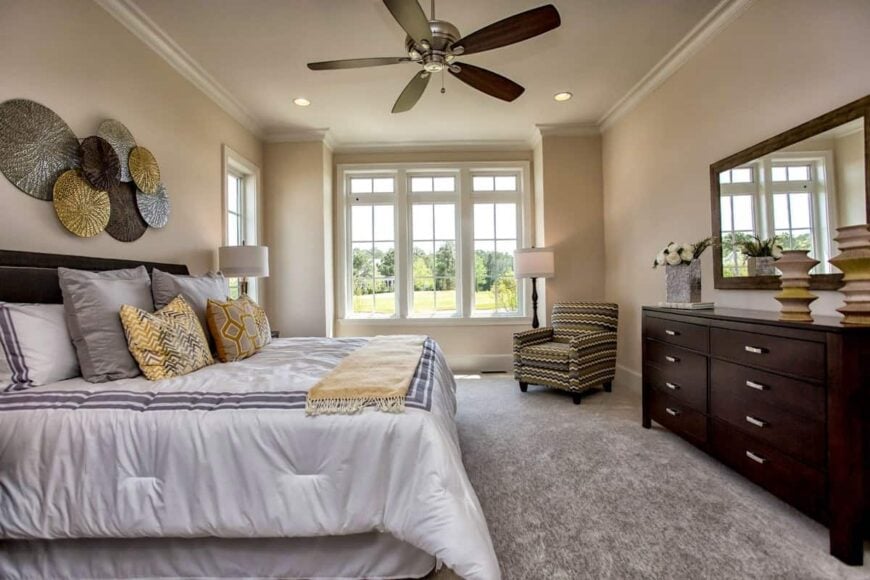 The primary bedroom has a striped armchair, a dark wood dresser, and a cozy bed adorned by round wall arts.