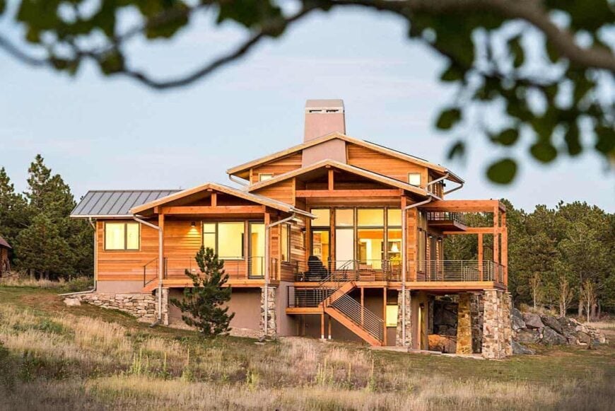 Side exterior view showing the multiple gables and a spacious deck supported by stone columns.