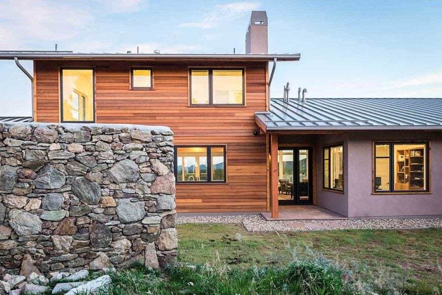 Rear exterior showing the stone retaining walls and a covered deck situated in between the wood cladding and concrete walls.