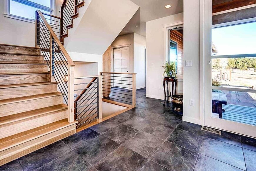 Foyer with a glazed entry door, a dark wood pedestal, and a wooden staircase.