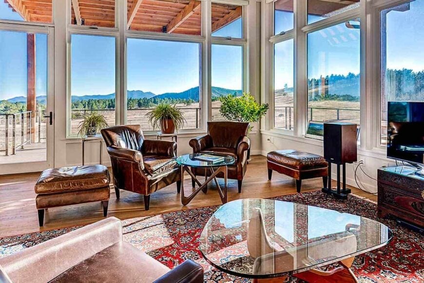 The great room has brown leather seats, glass top coffee tables, and a panoramic view of the magnificent mountains.