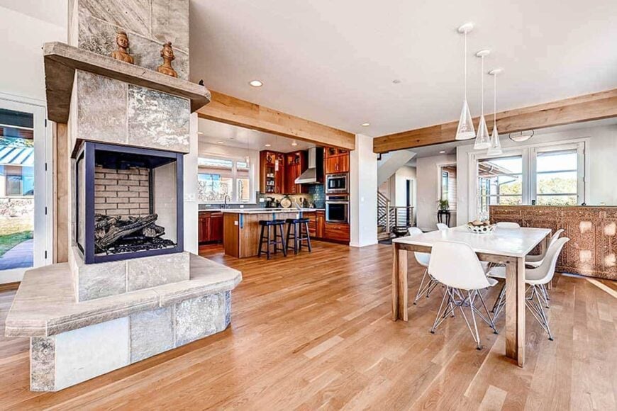 Dining area with white contemporary chairs and a wooden dining table illuminated by cone pendants.
