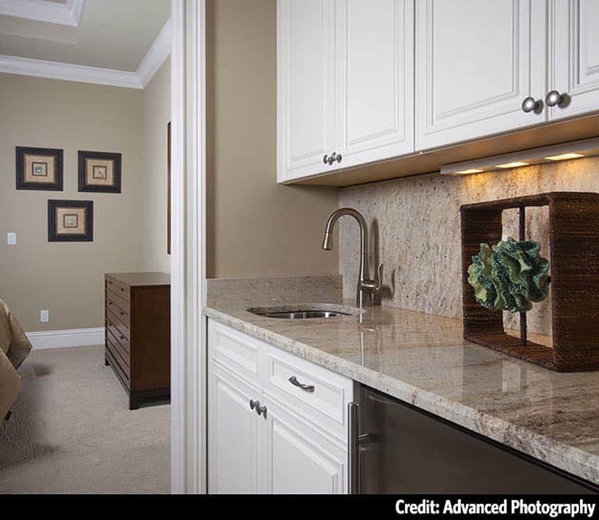 A closer look at the wet bar with white cabinets, granite countertops, and an undermount sink.