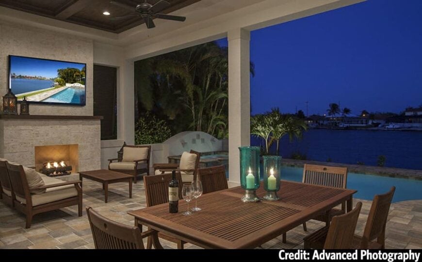 Covered lanai with wooden dining set, cushioned seats, and a fireplace with a wall-mounted TV on top.