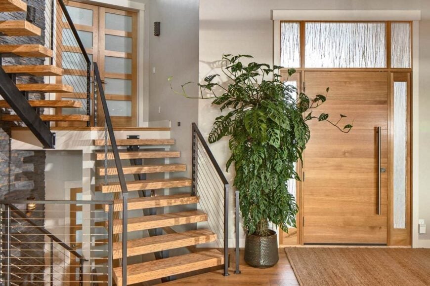 The foyer has a modern staircase, a tall potted plant, and a jute area rug.