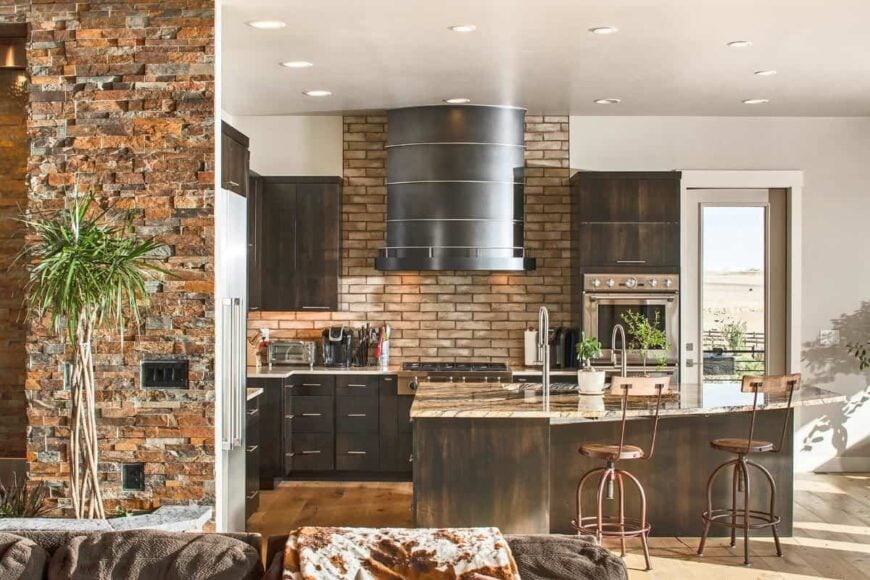 The kitchen has natural wood cabinetry, a brick backsplash, granite countertops, and a breakfast island.