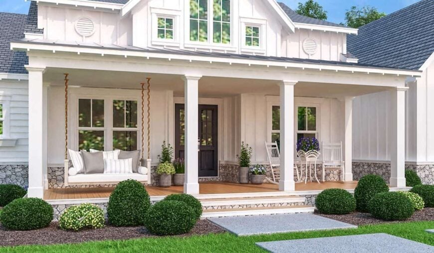 The covered front porch is filled with white rocking chairs, fresh potted plants, and a swinging bench filled with gray and striped pillows.