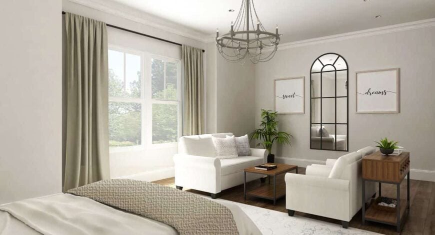 Primary bedroom with a cozy bed, a candle chandelier, and a sitting area adorned with an arched framed mirror and artworks.