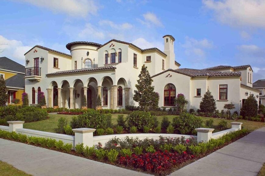 Angled front view showing the pristine stucco siding, tiled roofs, and open archways framing the covered porch.