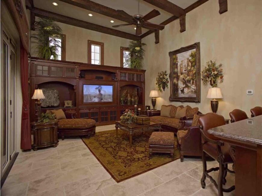 Gathering room with classic seats, wooden tables, red patterned rug, and a TV fitted on the built-in cabinet.