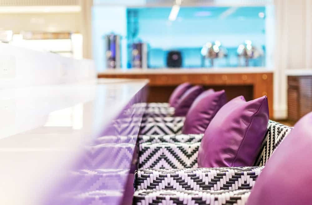 The long white table is paired with comfortable patterned armchairs that have purple cushions to complete the aesthetic.