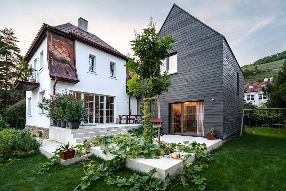 This is a close look at the back of the house with a large concrete structure that has steps and planters in between two different house exteriors.