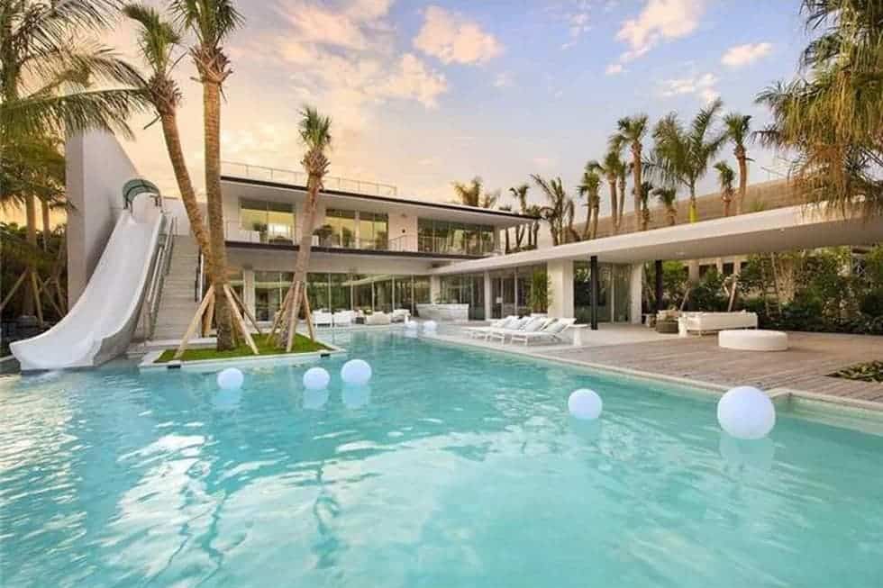 This is a view of the back of the house with a large swimming pool that is connected to the second level of the house with a water slide.