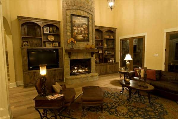 Brown leather seats, oval coffee table, stone fireplace, and wooden built-ins complete the living room.