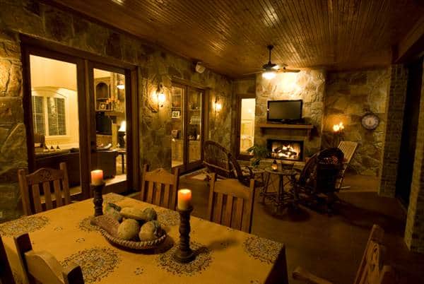 The covered porch is filled with a wooden dining set, wicker seats, a TV, and a cozy fireplace.