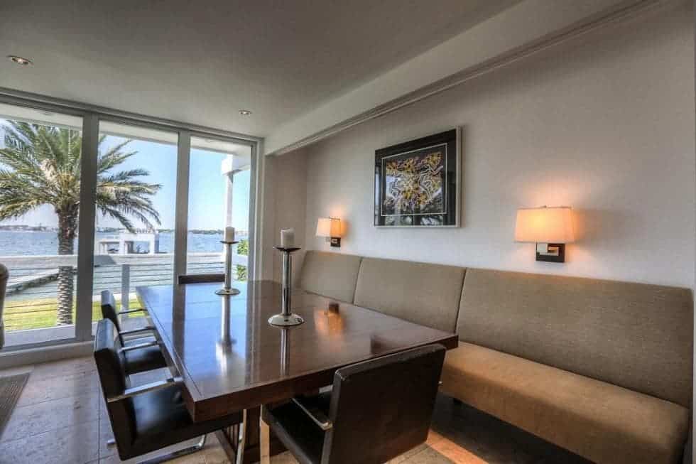 This is a close look at the dining area with a long dark wooden dining table paired with a built-in cushioned bench that is topped with sconces and a painting. Image courtesy of Toptenrealestatedeals.com.