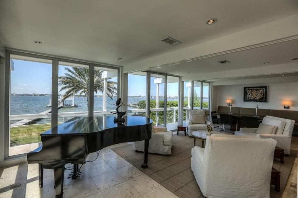 A few steps from the dining area is the family area with comfortable cushioned armchairs beside a grand piano that contrasts the brightness of the room. Image courtesy of Toptenrealestatedeals.com.