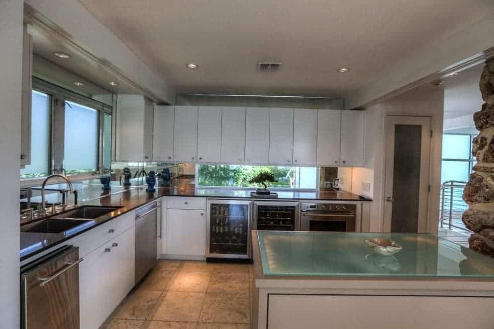 This is the kitchen with a peninsula on the side that has white cabinetry to match those lining the walls. These are complemented by the glass walls and appliances. Image courtesy of Toptenrealestatedeals.com.
