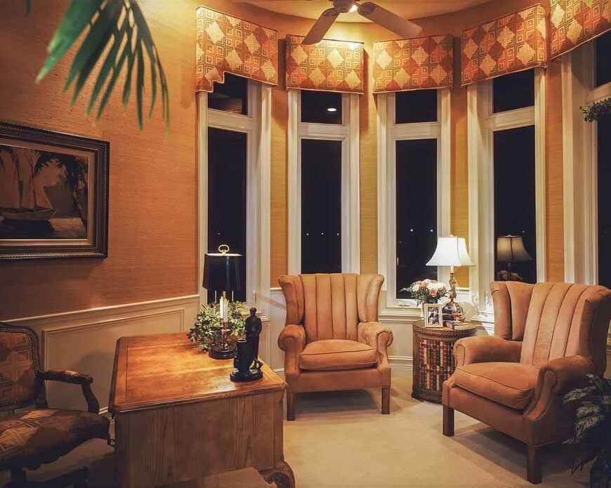 Study with cushioned seats, a wooden desk, and a bay window dressed in patterned valances.