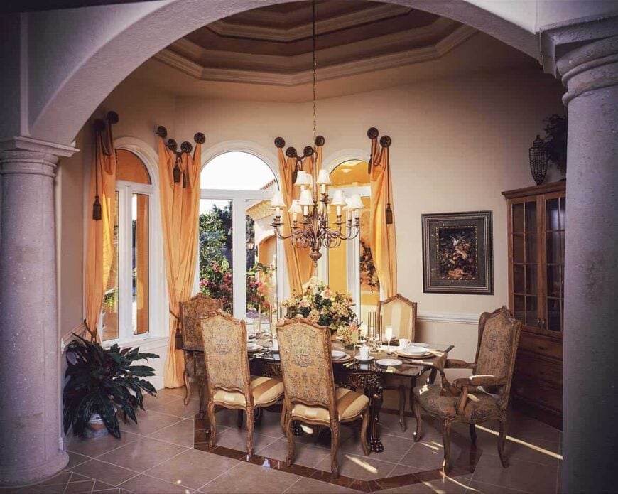 The formal dining room has classy chairs, a carved wood dining table, arched windows, and an ornate chandelier that hangs from the step ceiling.