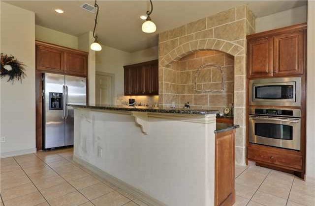 The kitchen is equipped with stainless steel appliances, a two-tier island, wooden cabinetry, and a cooking alcove.