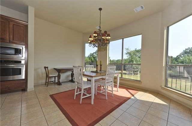 Dining room with wooden tables and chairs, an ornate chandelier, and a red area rug that lays on the tiled flooring.