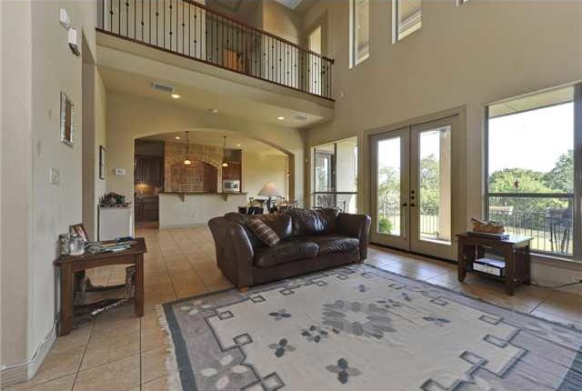 The living room has a leather sofa, wooden tables, a tasseled area rug, and a french door that leads out to the covered patio.