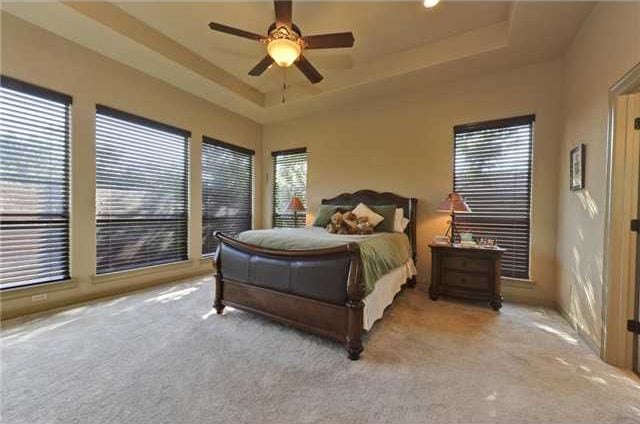 Primary bedroom with wooden furnishings, tray ceiling, carpet flooring, and plenty of windows covered in brown roller blinds.