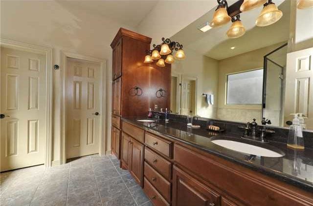 The primary bathroom features a long vanity with dual sink, black granite countertop, and warm glass sconces.