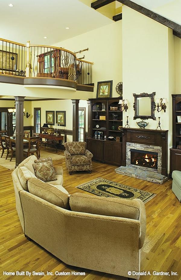 Living room with a curved sectional, patterned armchair, and a stone fireplace flanked by dark wood built-ins.