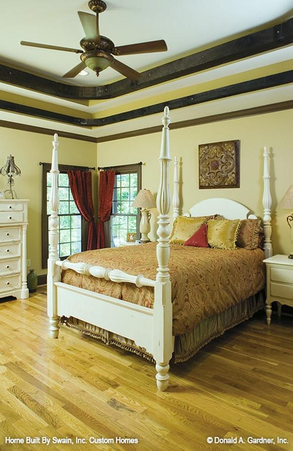 Primary bedroom with white furnishings, corner windows, hardwood flooring, and a striking step ceiling.