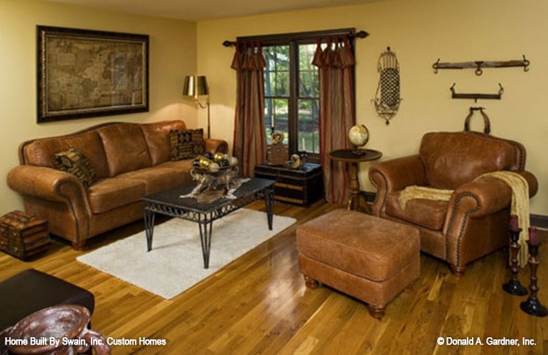 The second-floor loft is filled with brown leather seats, a metal console table, and a framed window dressed in flowy curtains.