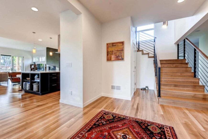 Foyer with a red printed rug and a wooden staircase that blends in with the hardwood flooring.