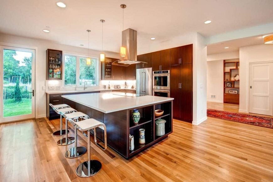 The kitchen is equipped with stainless steel appliances, marble countertops, dark wood cabinetry, and an immense breakfast island.