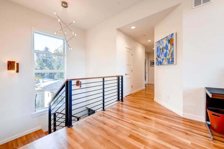 Second-floor loft with hardwood flooring, wrought iron railings, and a contemporary chandelier.