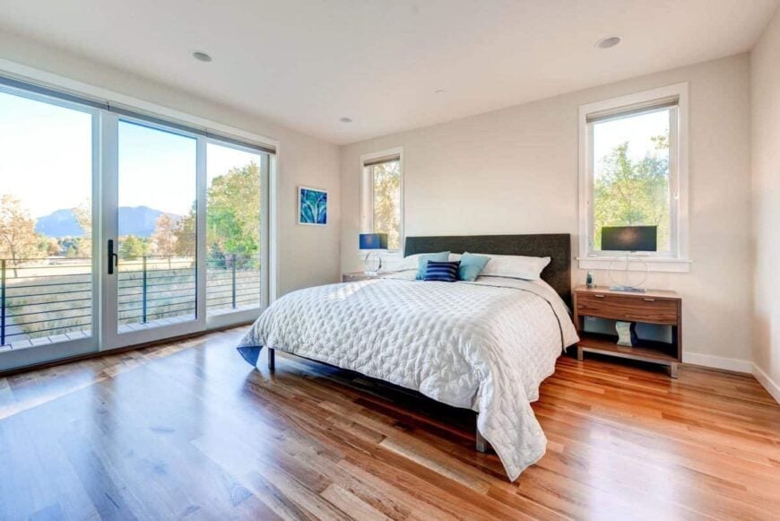 The primary bedroom has wooden furnishings, picture windows, and a glass door that opens to the balcony.