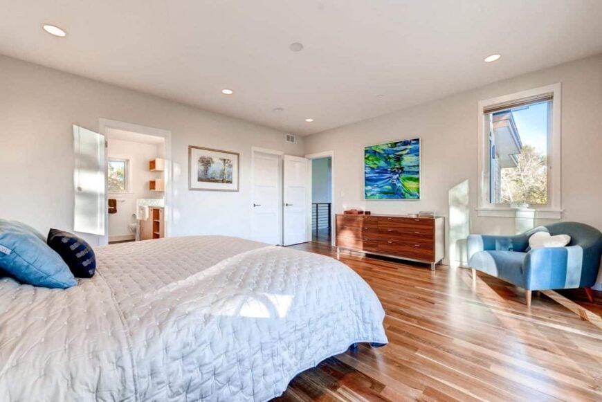 There's a blue armchair in front of the bed along with a wooden dresser and an abstract painting.