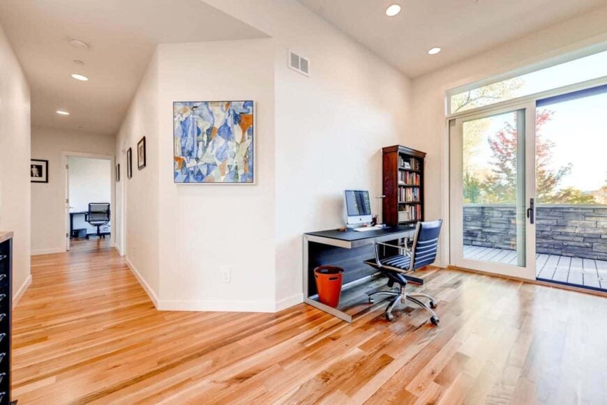 Study with a black desk, a leather swivel chair, wooden bookcase, and access to the balcony.