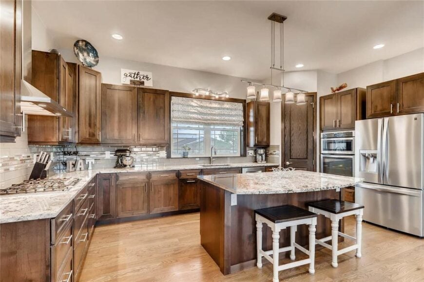 The kitchen is equipped with granite countertops, stainless steel appliances, wooden cabinetry, and a breakfast island.